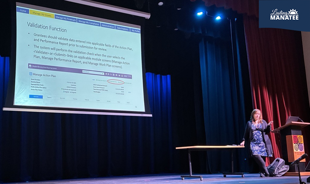 Instructor (Representative from HUD) standing before slideshow presentation in auditorium of venue for the HUD DRGR Conference in Ft. Lauderdale, FL