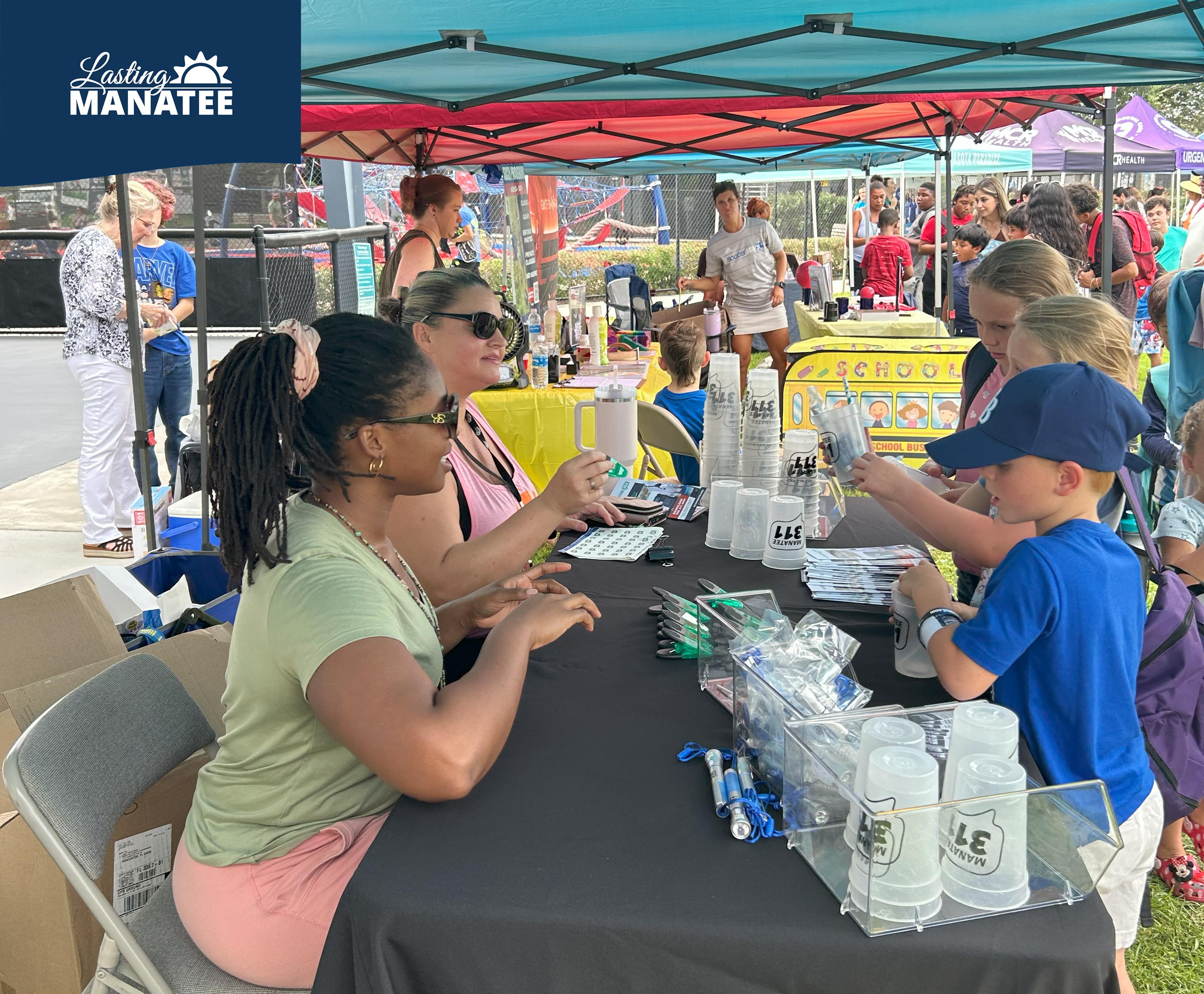 Staff from Lasting Manatee and Manatee 311 seated and helping children at vendor table at G.T. Bray Park for Family Fun Night - August 1, 2025