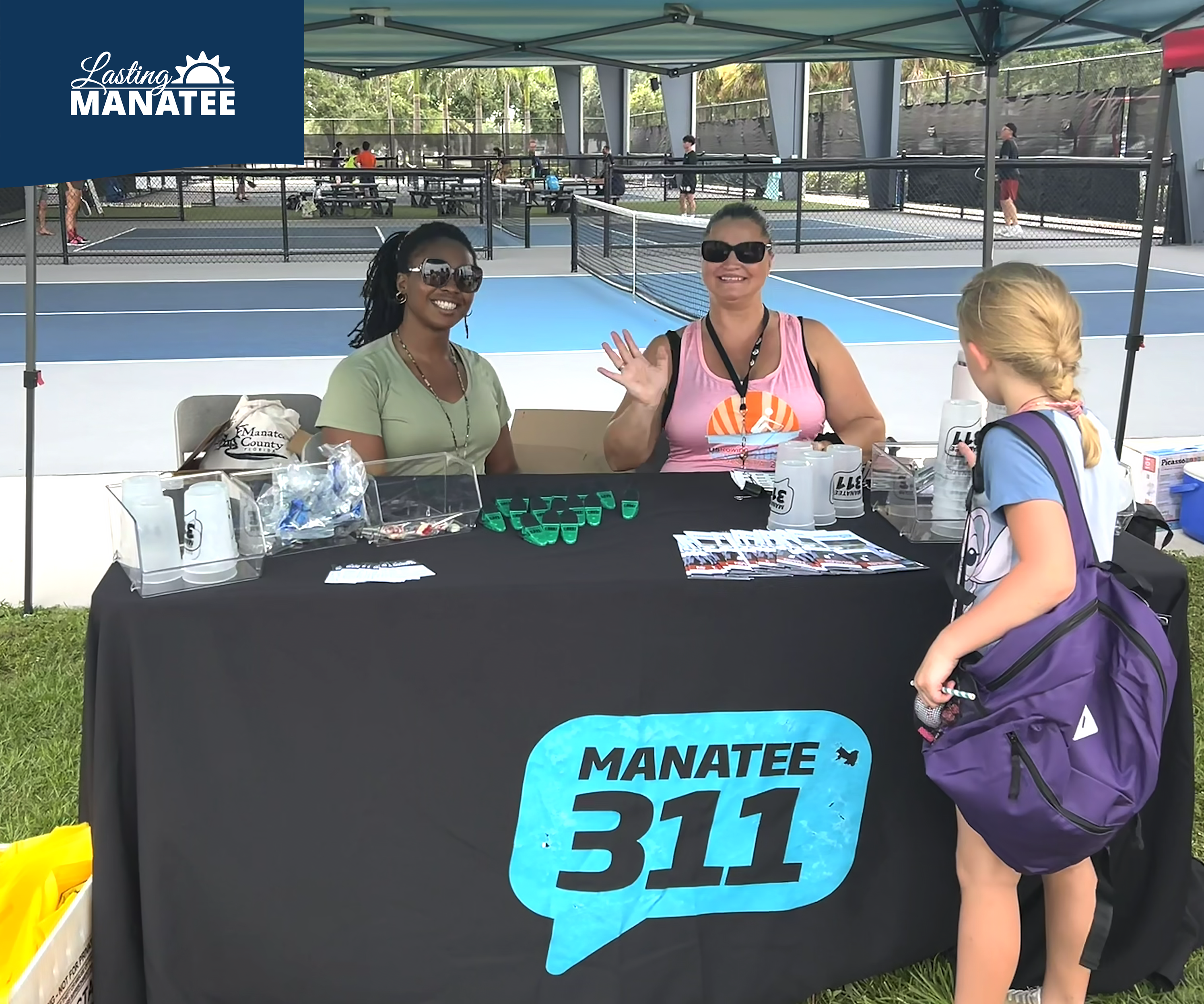 Staff from Lasting Manatee and Manatee 311 seated and helping children at vendor table at G.T. Bray Park for Family Fun Night - August 1, 2025